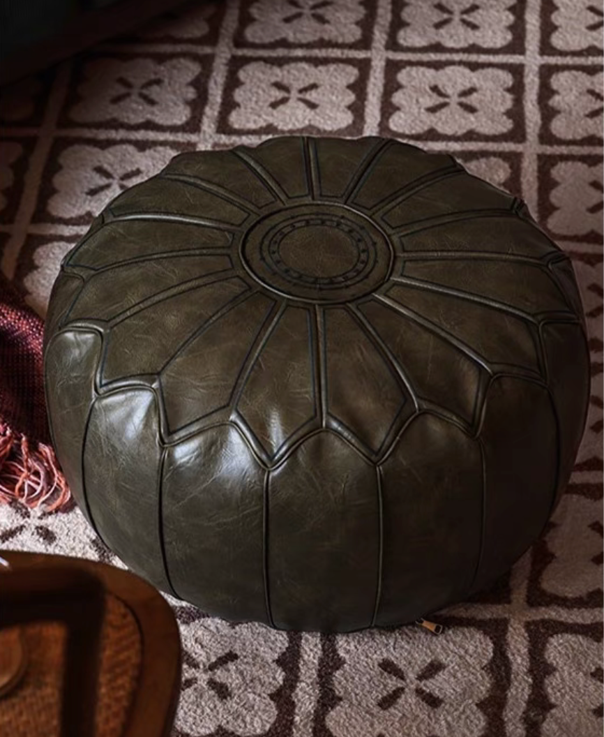 Olive green faux leather pouf ottoman placed on patterned rug in a warm living room setting