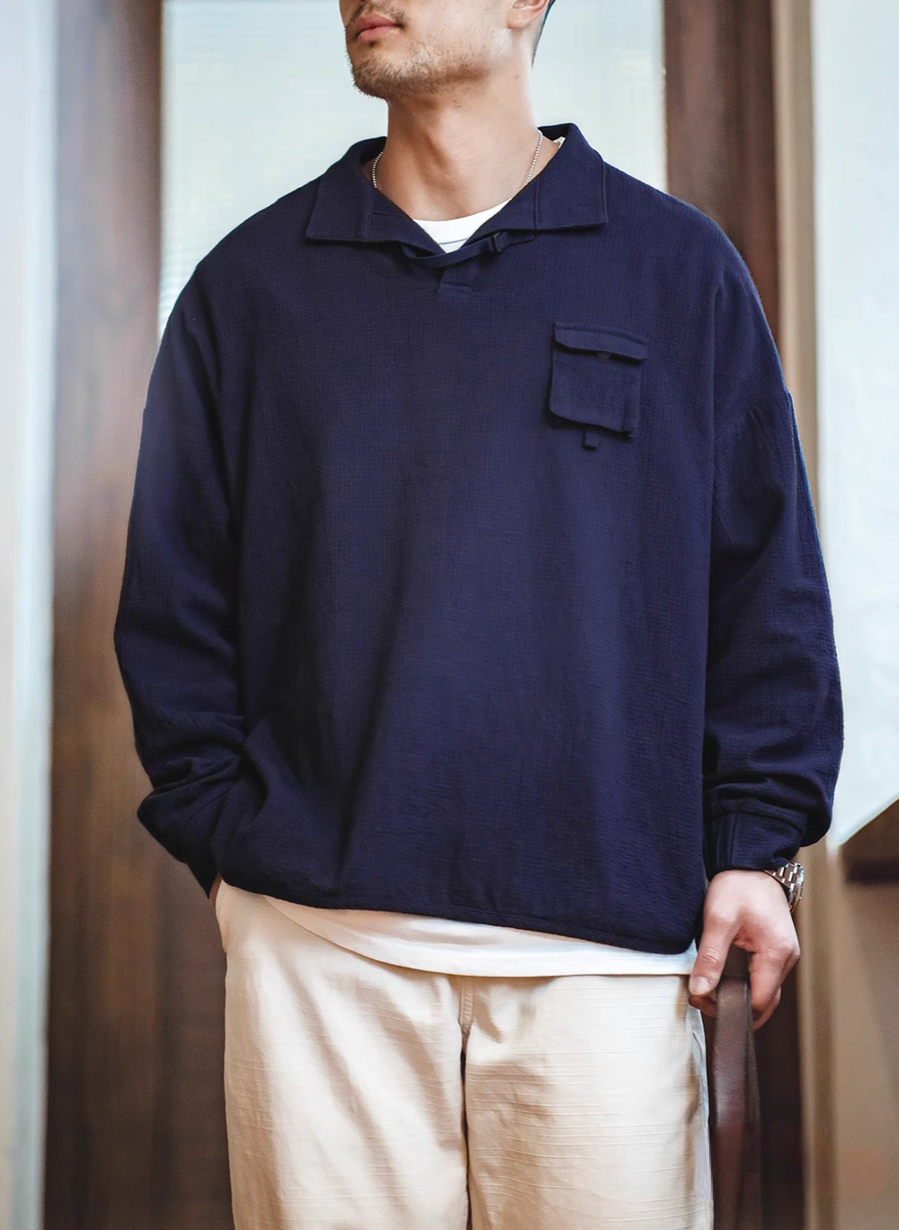 Blue textured cotton polo shirt worn by model front view showing relaxed fit, curved hem, and casual styling with light pants