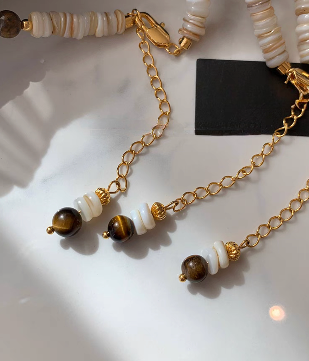 Close-up of tiger eye beads and shell disc beads with 24K gold-plated brass clasp and extension chain detail on choker necklace