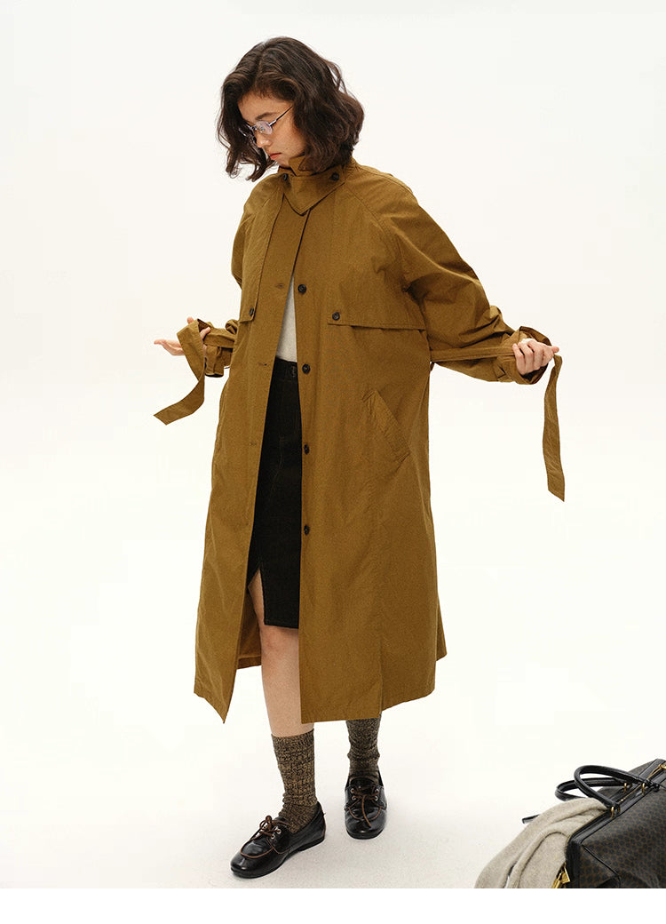 Woman adjusting the belt of a maple brown trench coat while looking down.