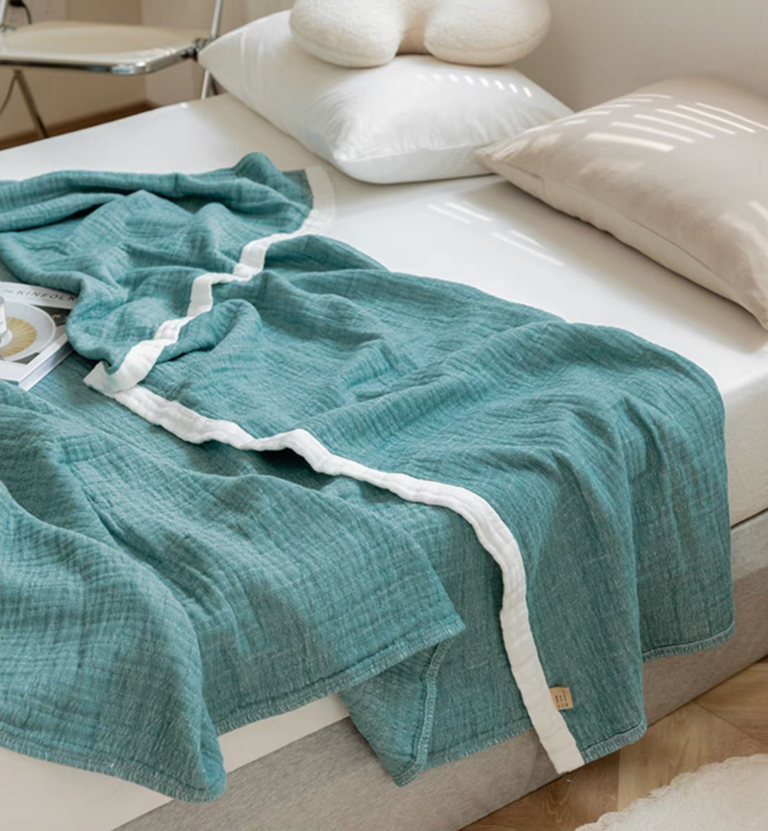 Dark green ripple gauze cotton quilt draped across bed corner showing zigzag stitched border.