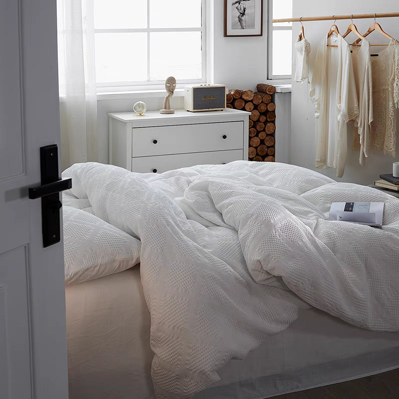 White ultra-soft organic cotton waffle weave bedding set draped on bed in bright minimalist bedroom