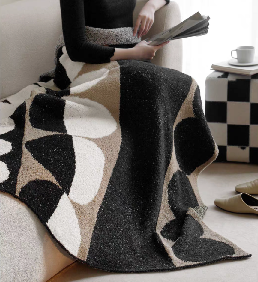 Black geometric circle throw blanket wrapped around seated person, showing soft plush texture and modern style