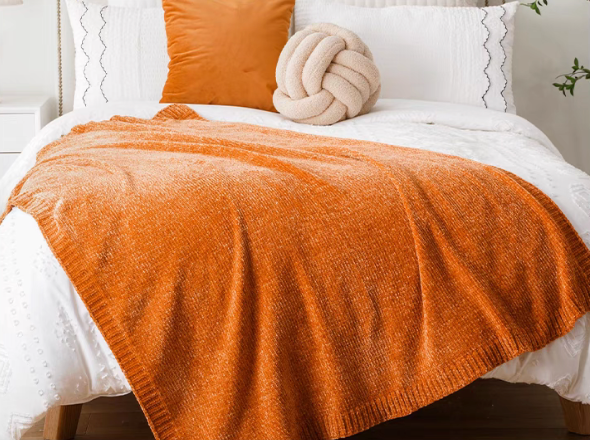 Orange vertical rib chenille knit solid throw blanket layered across a white bed