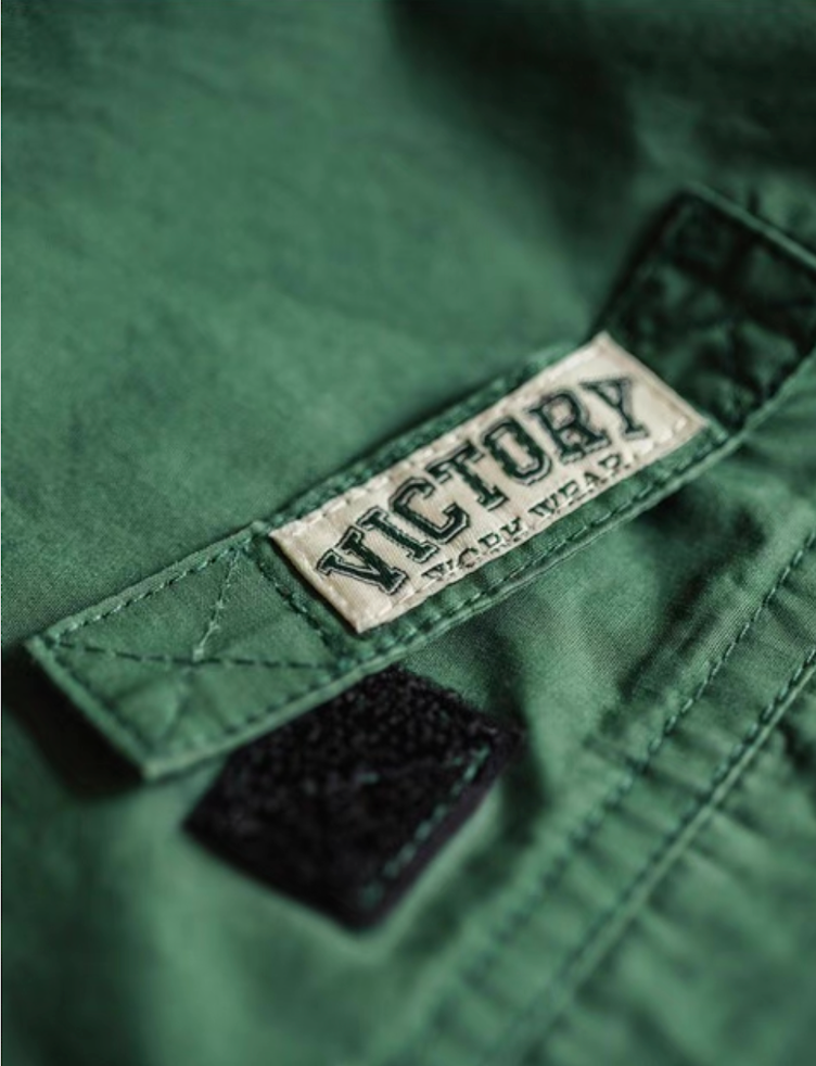 Macro shot of embroidered “Victory Work Wear” logo on hunter green shirt pocket