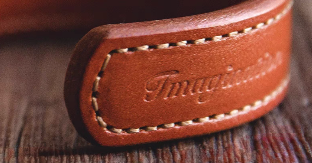 Dark brown leather cuff bracelet close-up of imagination embossed logo and hand stitched edge detail