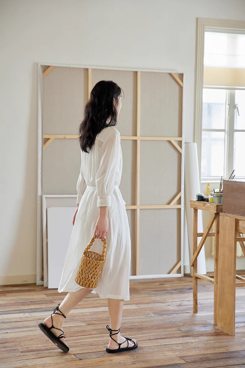 Back walking view of White pleated midi dress with woven bag, showing flowing hem, airy movement, and relaxed elegant styling
