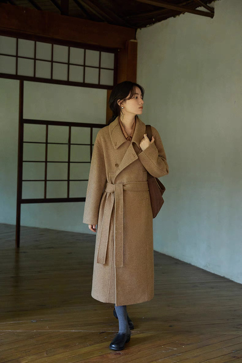 Full body view of woman wearing khaki long Willow Lane Wool Coat walking indoors, showcasing mid-calf length, belted waist, and effortless sophisticated style