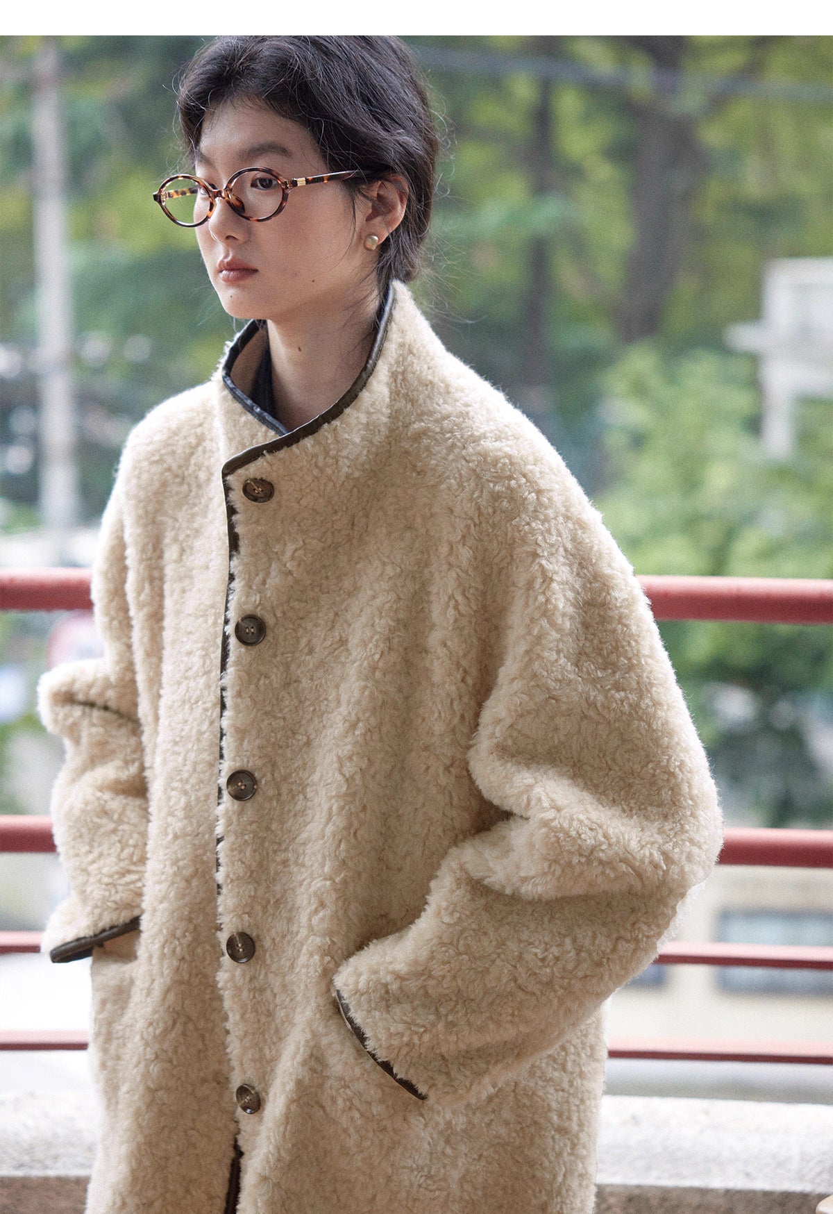 Woman in beige wool shearling coat with button front design and hands in pockets.