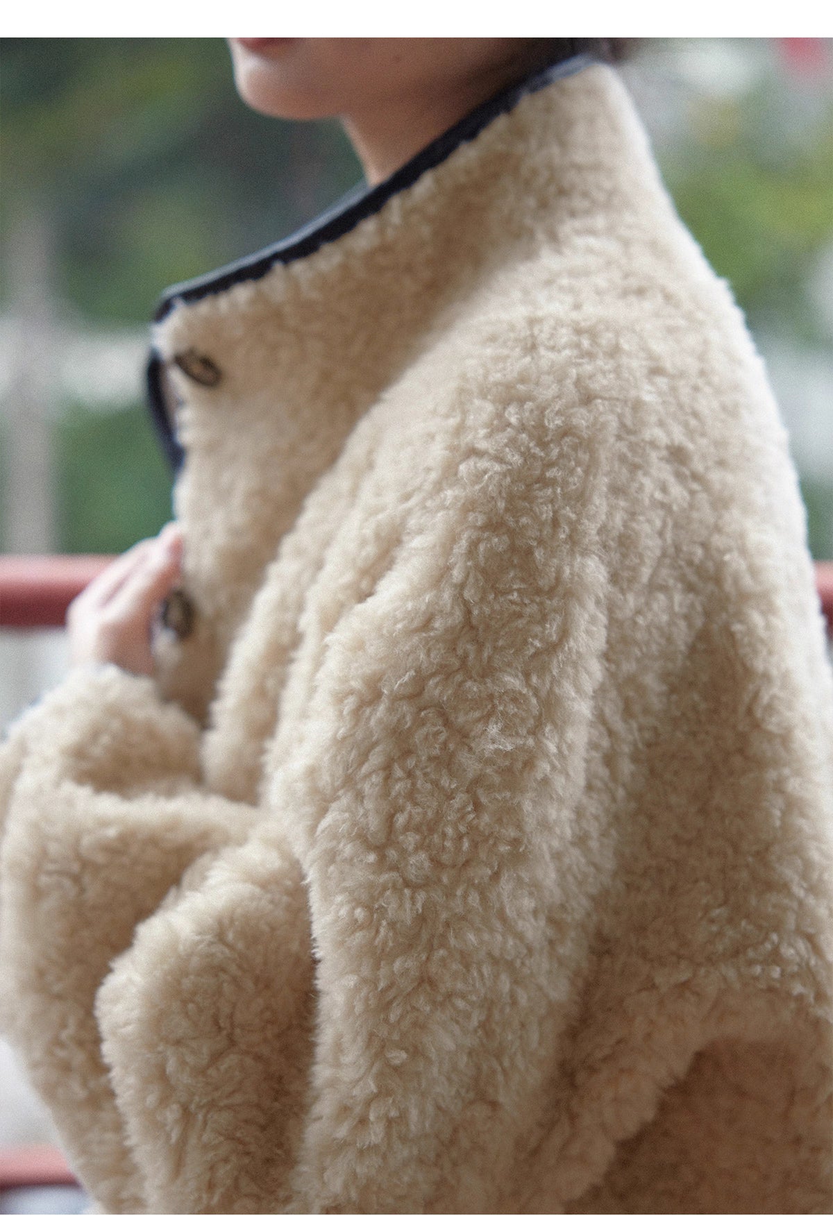 Close-up view of beige wool shearling coat showing soft textured fabric and high collar details.