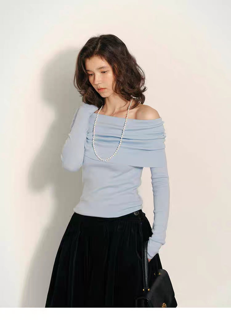 Soft sky-blue off-shoulder wool top styled with long sleeves and black skirt against a light wall