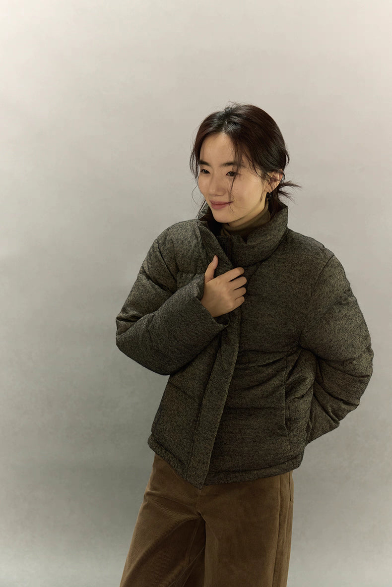 Woman standing in wool-blend down jacket with hands near collar.