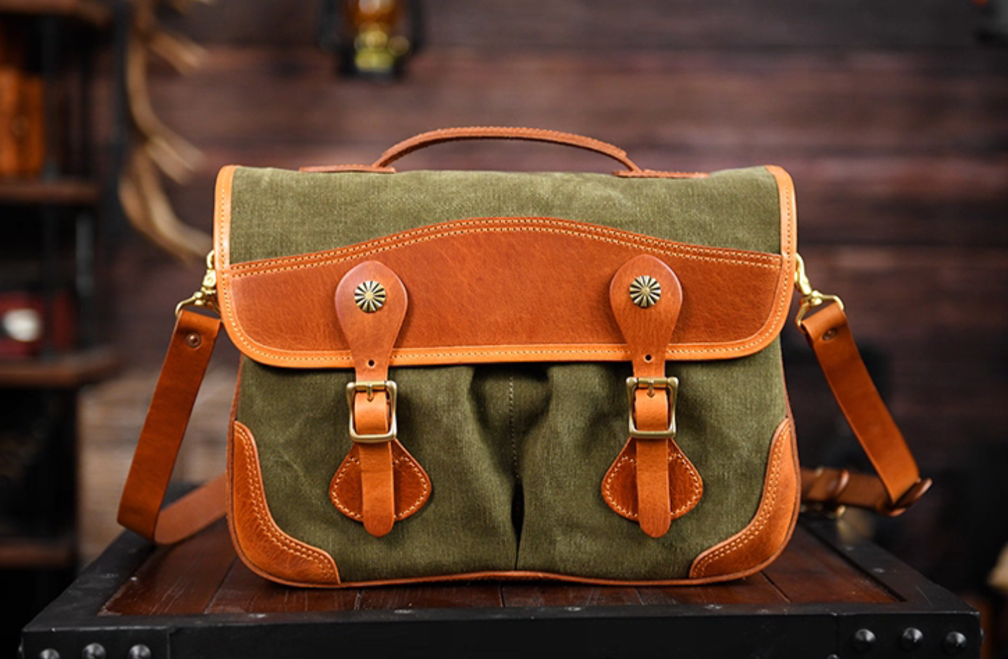 Front view of olive green waxed canvas satchel with tan leather trim and brass buckles