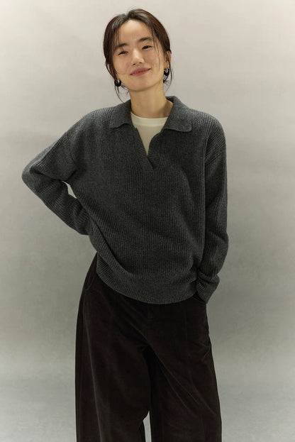 Model smiling in charcoal gray ribbed cashmere-wool polo sweater, relaxed fit with drop shoulders.