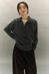 Model smiling in charcoal gray ribbed cashmere-wool polo sweater, relaxed fit with drop shoulders.