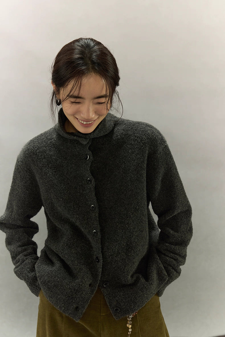 Model smiling while wearing dark charcoal wool high-neck cardigan with hands in pockets, showcasing cozy texture and relaxed fit.
