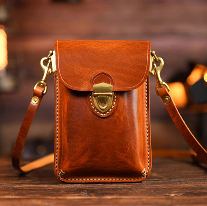 Amber brown leather crossbody pouch with brass lock, front view on wooden table.