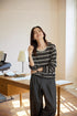 Model smiling in charcoal and oat striped Tencel-linen pullover, relaxed drape with rolled sleeves.