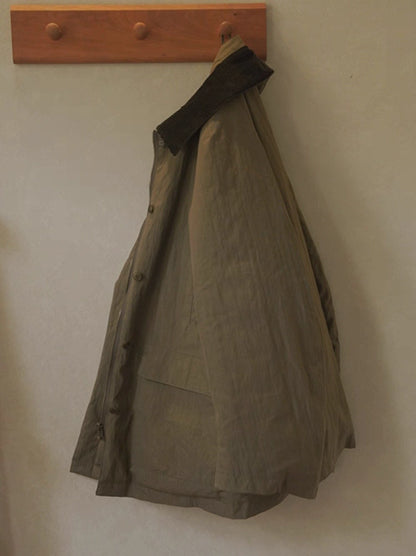 Army green outdoor down jacket hanging on wooden hook showing corduroy collar.