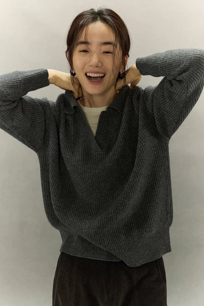 Woman laughing and adjusting collar in dark gray ribbed cashmere-wool sweater, showing soft drape.