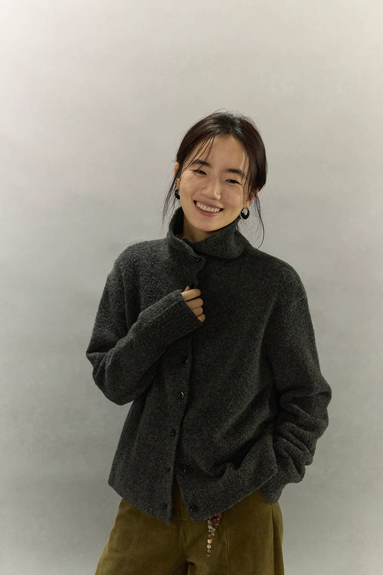 Woman wearing charcoal wool high-neck cardigan fully buttoned, showing relaxed drop-shoulder silhouette and warm texture.