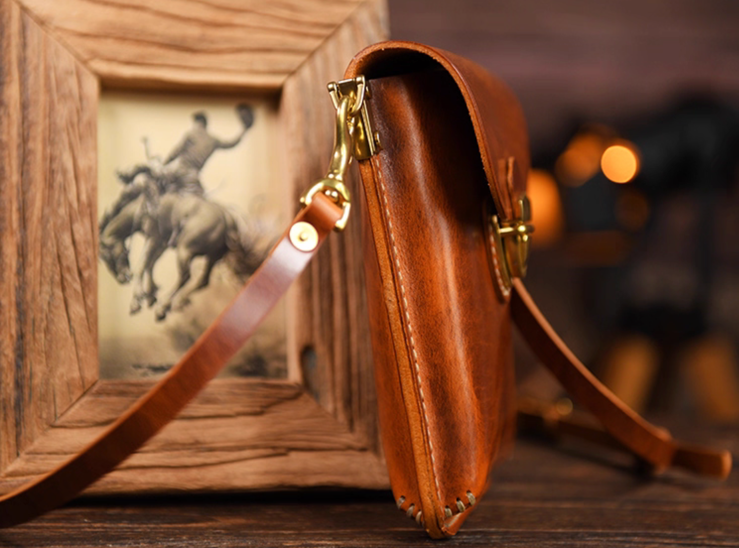 Side profile of slim amber brown leather pouch showing detachable strap and brass hardware.