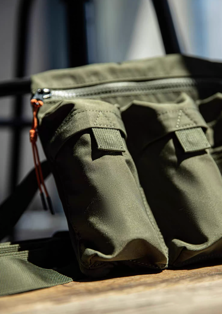 Close-up of army green crossbody bag cargo pockets with zipper and flap details