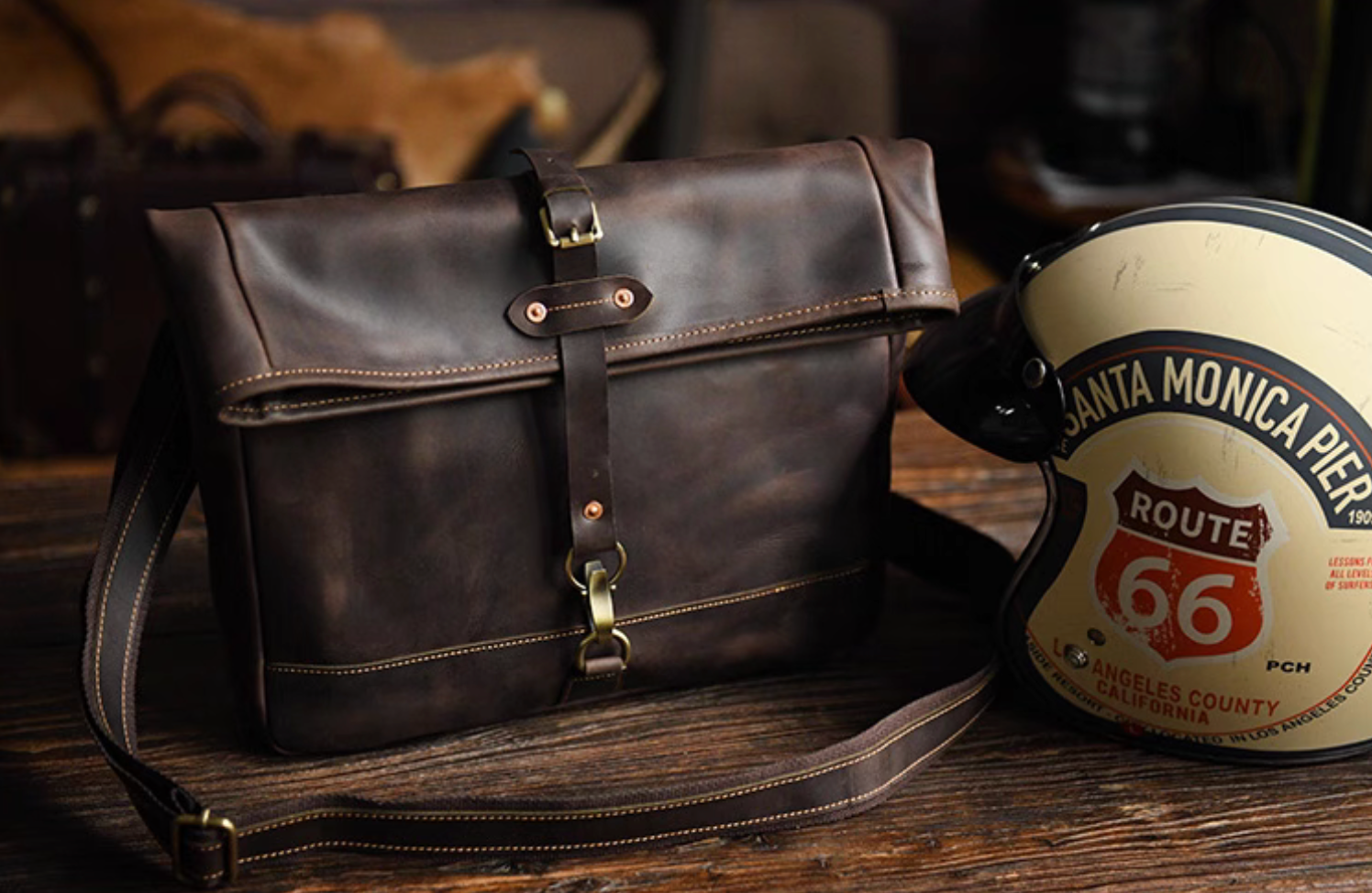 Angled view of full-grain leather satchel beside Route 66 helmet, showing vintage travel style