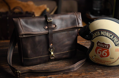 Angled view of full-grain leather satchel beside Route 66 helmet, showing vintage travel style