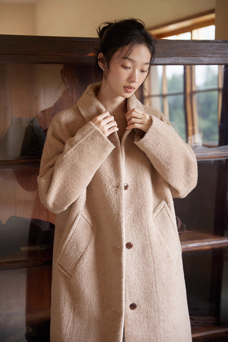 Close-up of model adjusting the collar of an oat beige Suri alpaca wool coat.