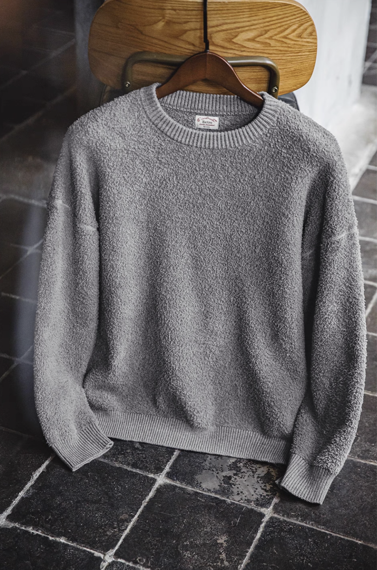 Light grey fleece knit sweater displayed on a wooden chair with warm indoor lighting