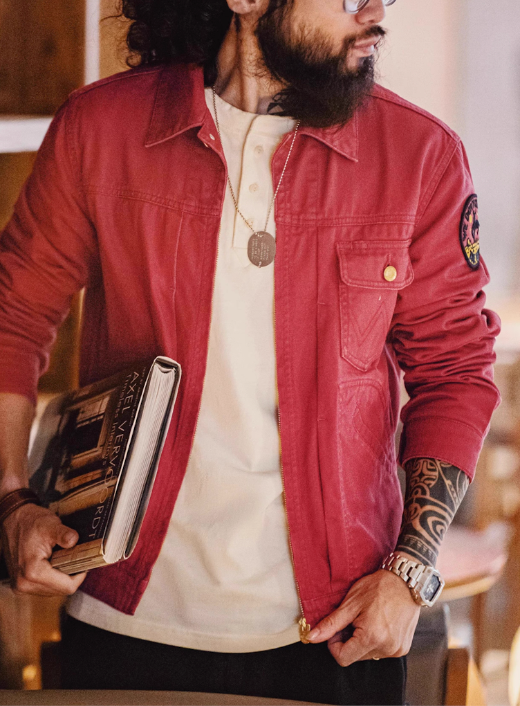 Man wearing rust red rodeo jacket over cream tee holding book indoors