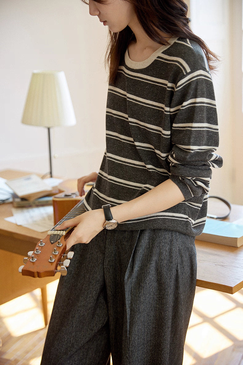Woman holding a guitar while wearing charcoal and oat striped Tencel-linen sweater, cozy and casual.