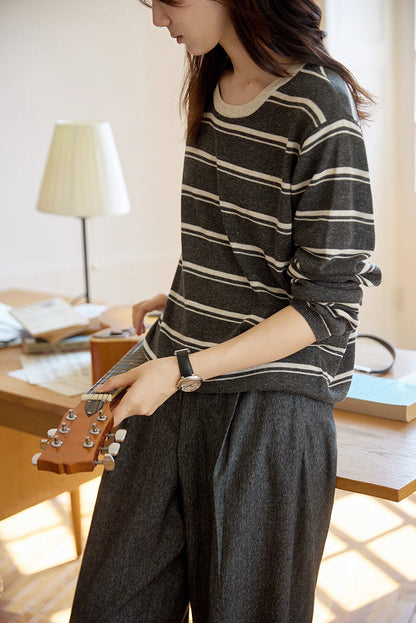 Woman holding a guitar while wearing charcoal and oat striped Tencel-linen sweater, cozy and casual.
