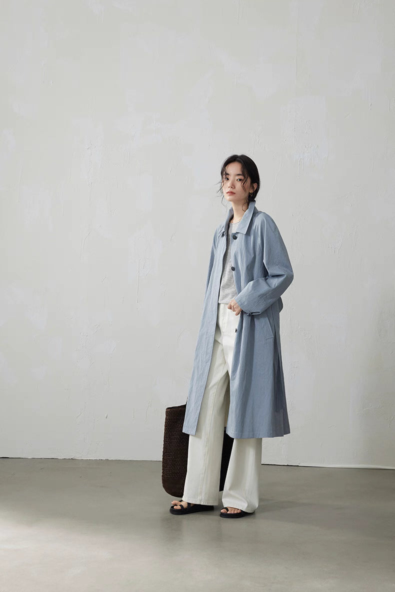 Light blue-gray A-line coat styled with layered outfit and woven tote bag.