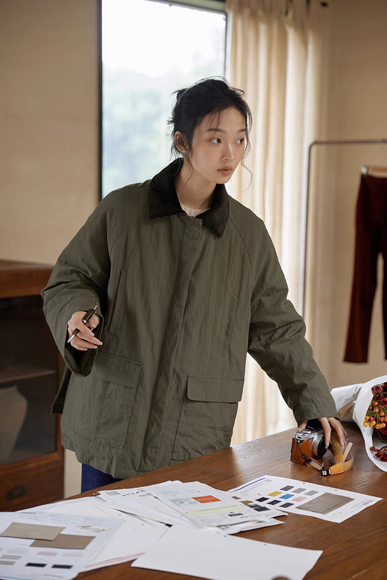 Model in army green heritage down jacket standing by table with fabric swatches.
