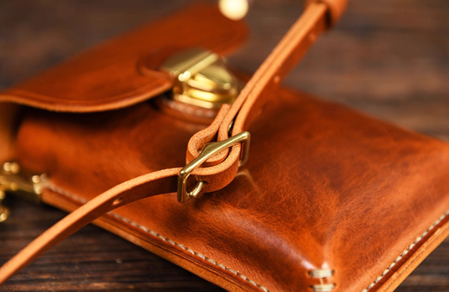 Close-up of leather shoulder strap and brass buckle on handcrafted leather crossbody pouch.