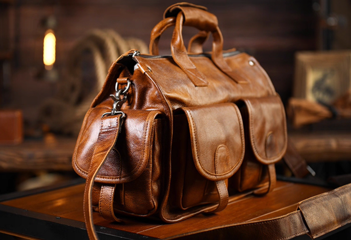 Side angle of camel leather duffle work bag showing strap and pocket details
