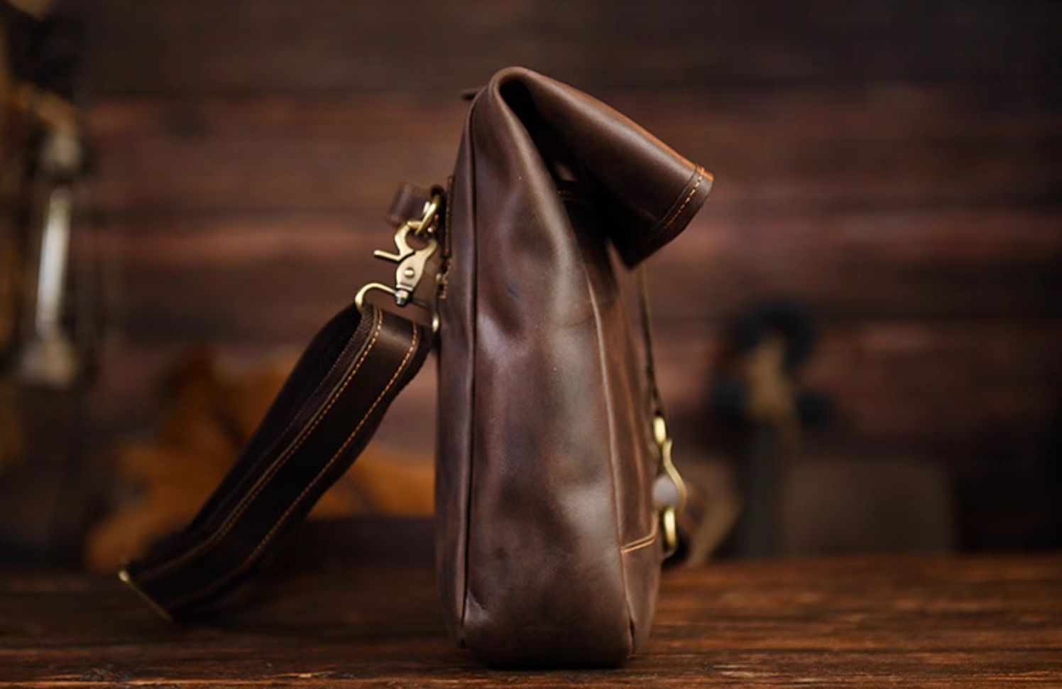 Side profile showing the thick leather texture and brass hardware of the messenger bag