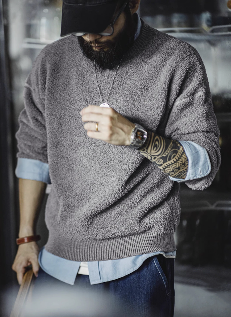Man wearing light grey fleece knit sweater layered over blue shirt with visible tattoos