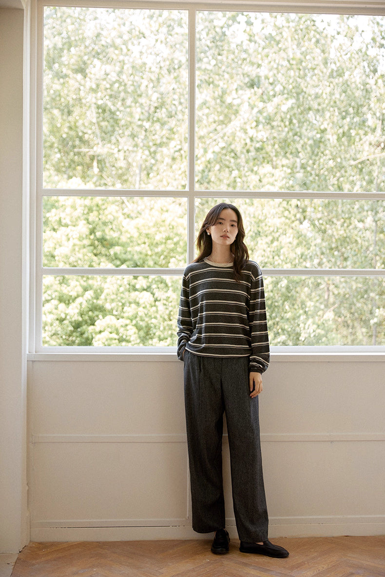Full-body view near window in charcoal and oat striped pullover, showing relaxed silhouette.