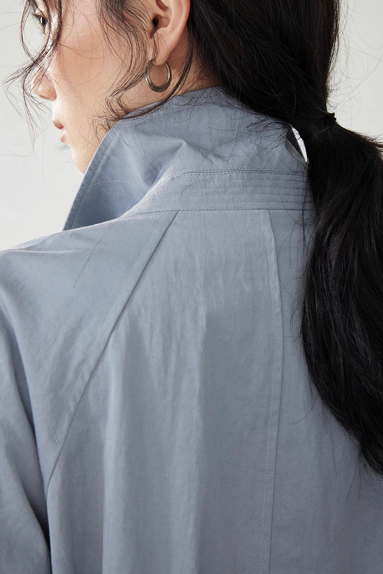 Close-up of collar stitching and raglan construction on light blue-gray trench coat.
