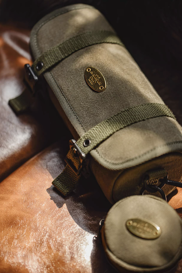Close-up of olive canvas barrel bag with brass plate on leather chair