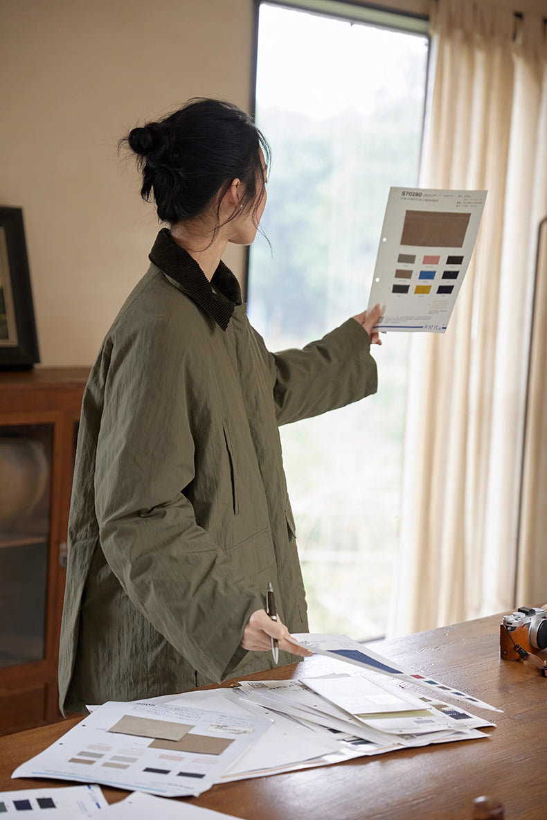 Model holding fabric color chart while wearing army green outdoor down jacket.