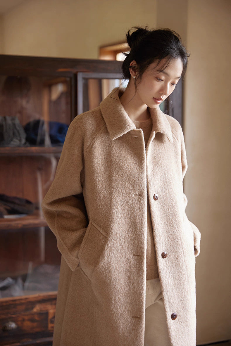 Close-up shot of the alpaca coat texture as the model looks downward by a window.