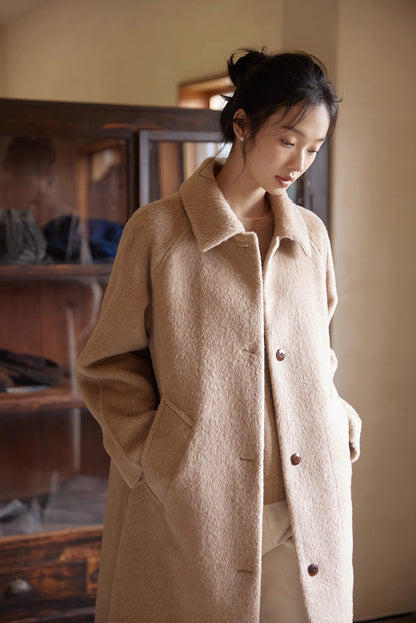 Close-up shot of the alpaca coat texture as the model looks downward by a window.