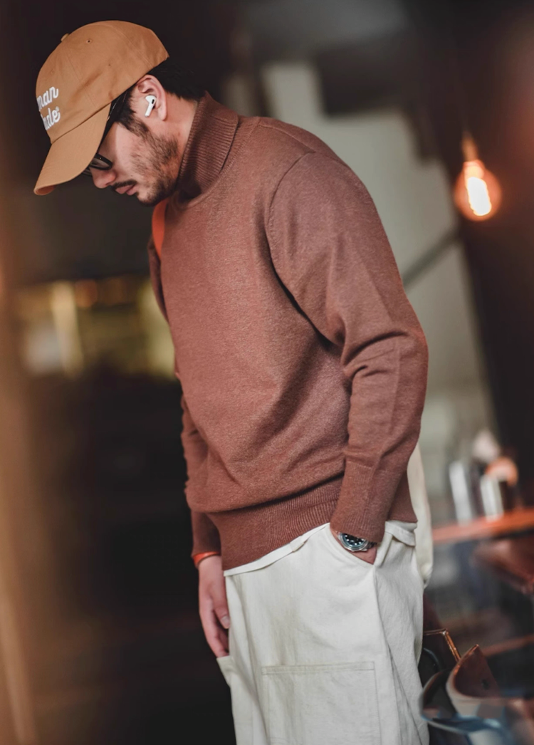 Man in mocha brown turtleneck and beige cap posing in relaxed indoor scene