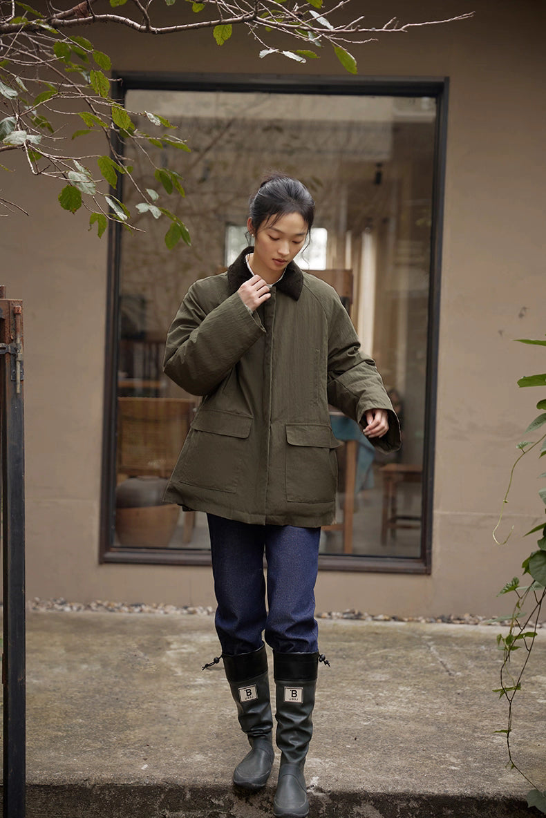 Model wearing army green down jacket and boots walking outdoors on patio.