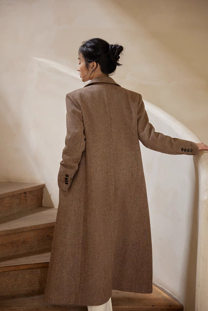 Back view of a woman walking upstairs wearing a long brown herringbone wool coat.