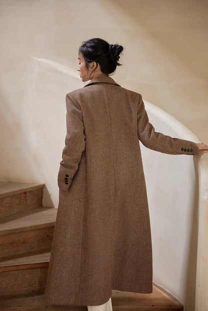 Back view of a woman walking upstairs wearing a long brown herringbone wool coat.